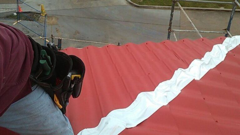 1. A roofing specialist performing a quick roof leak repair on a red metal roof, sealing the joint for better protection.