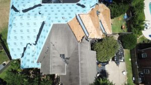 Houston home undergoing partial roof repair with visible blue underlayment and debris collection setup.