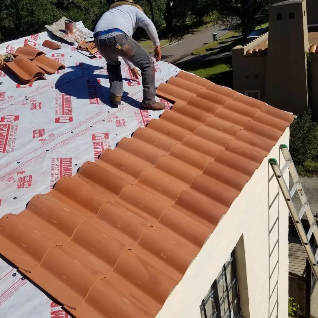 Roofing contractor installing red clay Spanish tiles during a residential roof installation by Achilles Roofing & Exterior