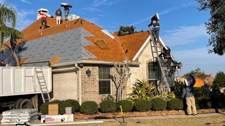 A high-activity residential roofing site showing multiple crew members simultaneously working on a full roof replacement. Workers are seen carrying materials up ladders and installing new brown asphalt shingles and gray underlayment. This image highlights the scale and coordination necessary for a professional project, emphasizing the complexity that amateur work often overlooks, leading to costly roof repair mistakes.