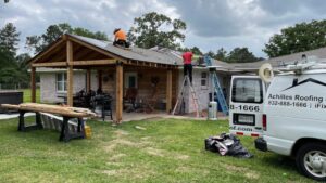 A residential property where roof replacement is underway on both the main house and an attached patio structure. The presence of the clearly marked "Achilles Roofing" van and team members on ladders signifies a professional, licensed operation. This image encourages homeowners to choose established companies to avoid the typical project and warranty roof repair mistakes associated with unqualified workers.