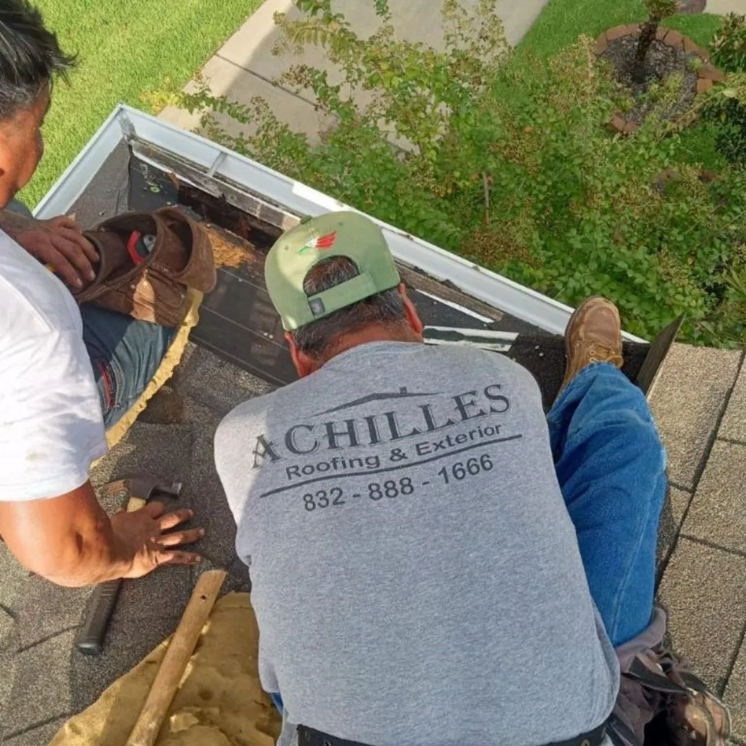 Achilles Roofing & Exterior technician in a branded shirt performing an emergency roof repair on a shingle roof in Houston.