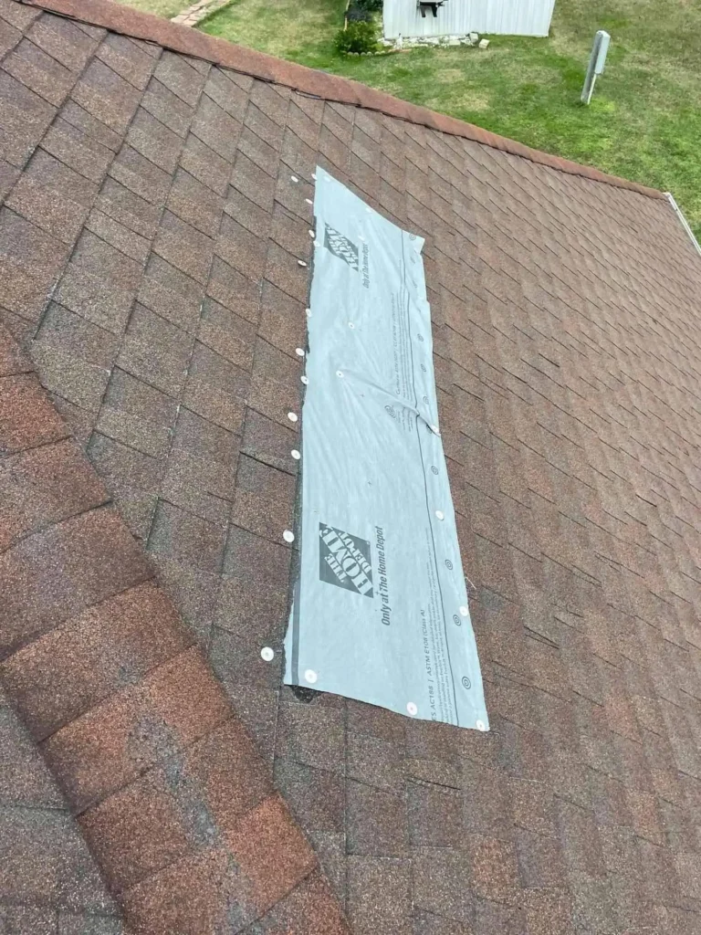 In this image, the house’s roof displays damaged shingles under a makeshift wrap, revealing the need for a full roof repair.