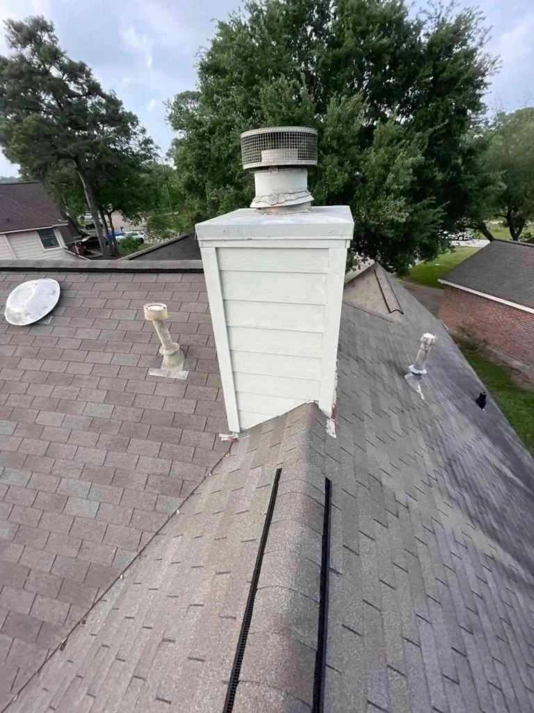 This image shows a dirty chimney and worn shingles on a Houston house prior to roof replacement, illustrating the aged roof condition before work begins.
