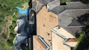 Aerial view of a residential roofing project in Cypress, TX showing exposed plywood decking and shingle removal.