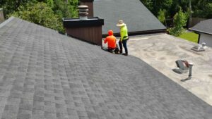 Two roofing professionals inspecting the transition between dark grey asphalt shingles and a flat roof membrane near a chimney.