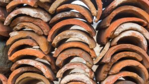 Close-up stack of weathered, barrel-shaped terracotta clay tiles showing natural texture and orange-brown earth tones.