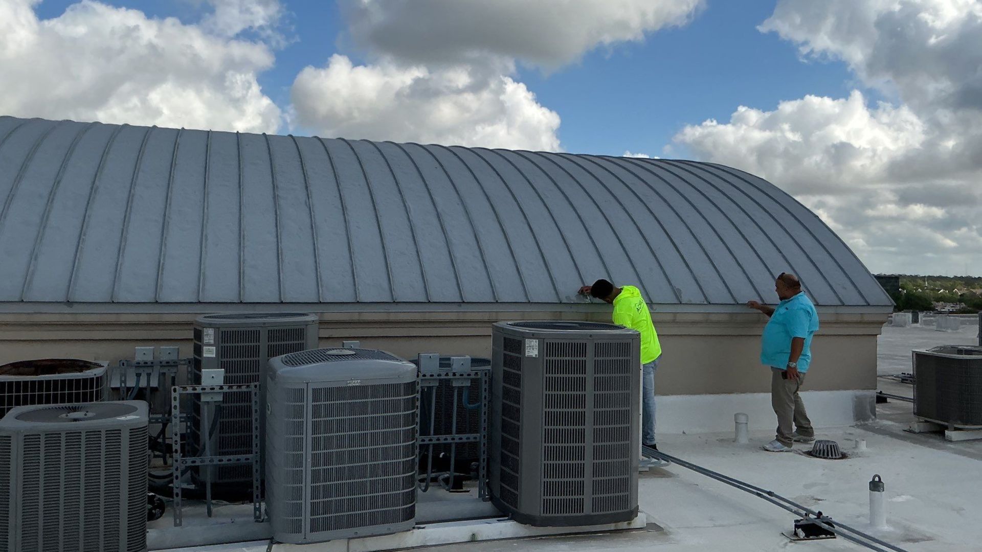 Achilles Roofing Houston field supervisors verifying curved metal roof seams and perimeter counter flashing parameters near mechanical equipment.