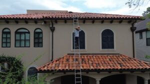 A professional roofing contractor installing classic terracotta barrels on a Spanish tile roof under a bright blue sky.