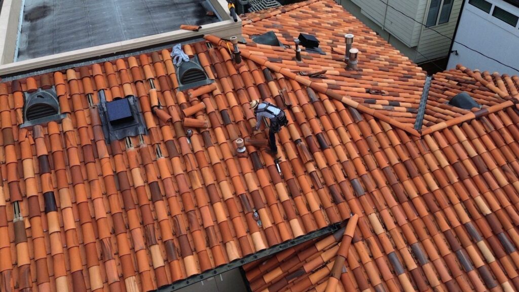 A beautiful close-up of overlapping terracotta shingles with a bold blue banner that reads "THE ULTIMATE GUIDE TO SPANISH TILE ROOF." Spanish Tile Roof Costs