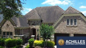 A luxury multi-gabled brick residence featuring a weathered brown concrete tile roof, with the Achilles Roofing & Exterior logo in the bottom right corner.