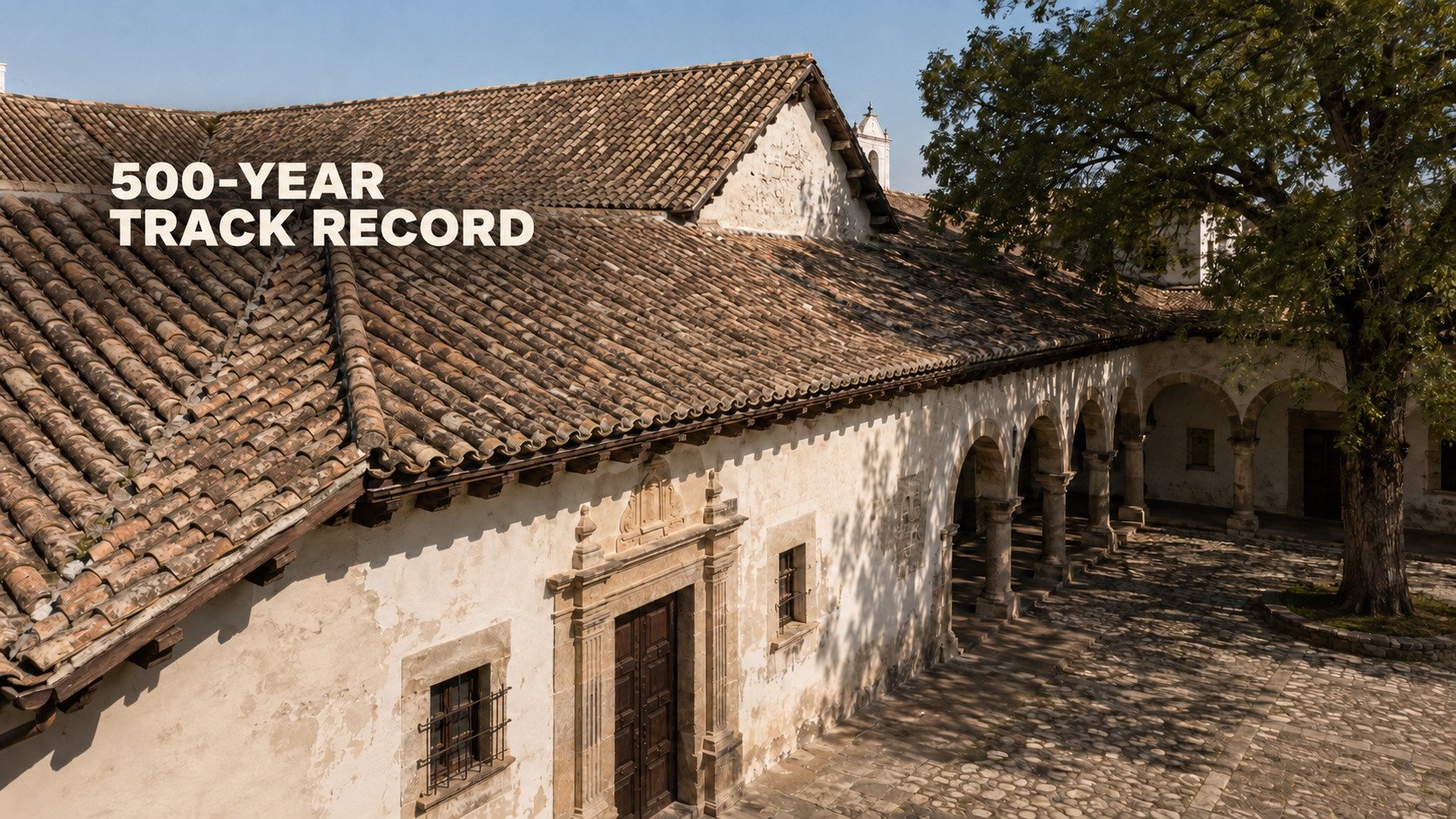 An historic stone building featuring an original weathered clay barrel tile roof, highlighting the longevity of premium Spanish tile roofing by Achilles Roofing.
