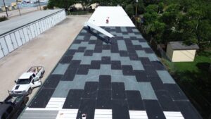 Workers installing ISO insulation boards and fastening new white panels on a commercial metal roof retrofit Baytown project by Achilles Roofing