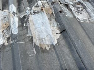 Damaged old commercial metal roof retrofit Baytown project site showing layered tape, fabric patches, cracked sealant, and rusted fasteners before repairs